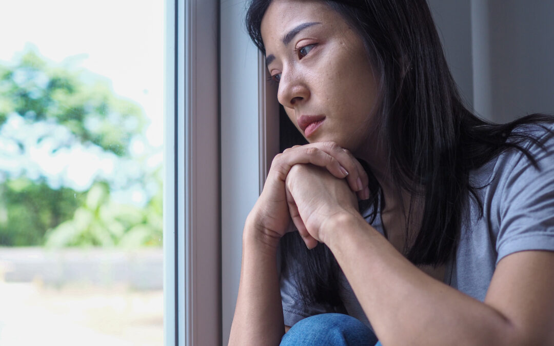 Young woman feeling sad, experiencing seasonal depression while looking out a window, pondering loneliness and mental health challenges during a melancholic season.